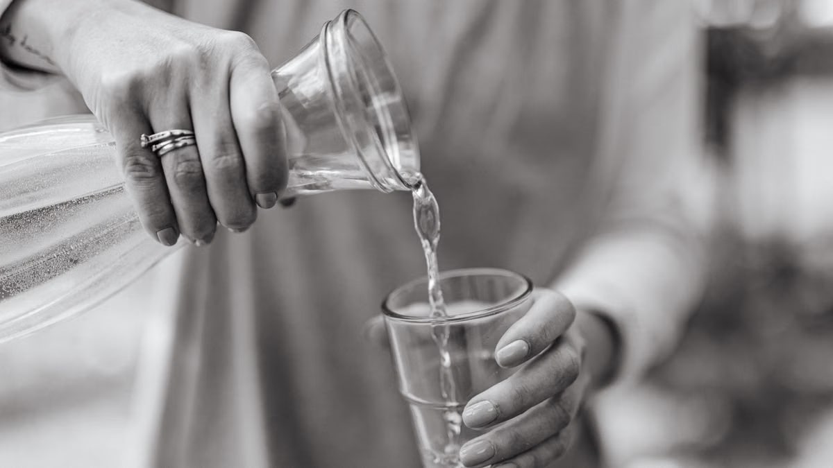 A close-up view of a woman pouring water from a carafe into a glass, highlighting hands and jewelry.